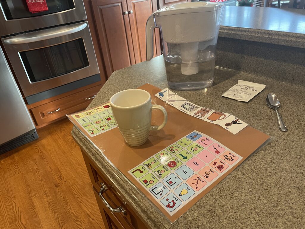 Communication placemat with hot chocolate supplemental symbols, mug, spoon, water pitcher, and hot chocolate packet.  