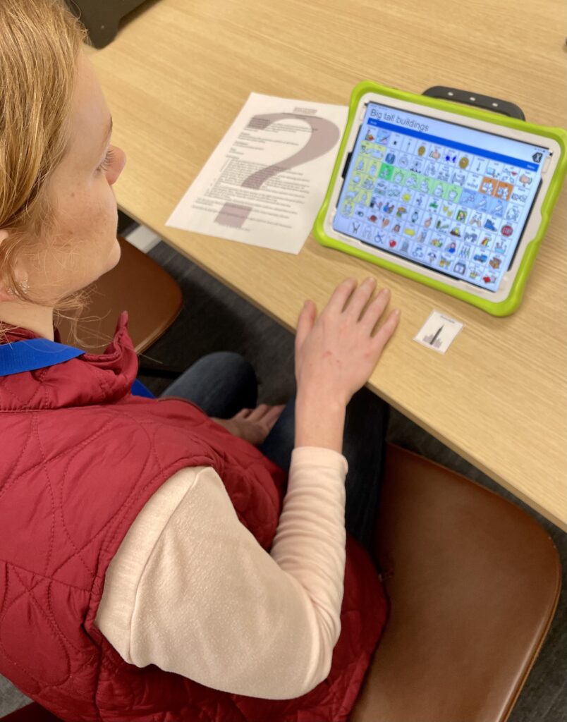 Teacher giving clues using a speech generating device during the Guess Me game.