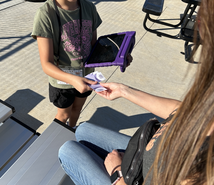Young girl handing a card to an adult sitting in bleachers.